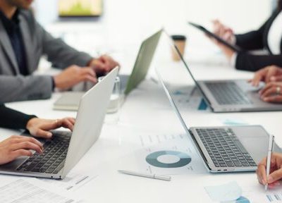 People working on laptops and reviewing documents around a conference table in an office setting.