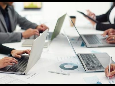 People working on laptops and reviewing documents around a conference table in an office setting.